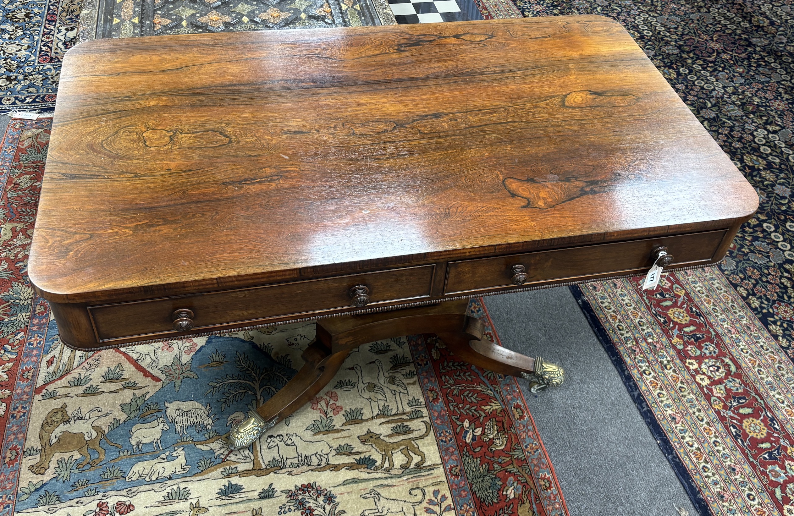 A Regency rectangular rosewood centre / library table, fitted two frieze drawers and two dummy drawers on single square tapered support, quadrapartite slab base and splayed legs with brass castors, width 123cm, depth 70c